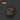 A black ceramic mug featuring a wrap-around graphic of various orange-handled tools hanging on a gray wall, shown on a dark gray background with concentric circles. An orange label in the top-left corner reads 'ORANGE'.