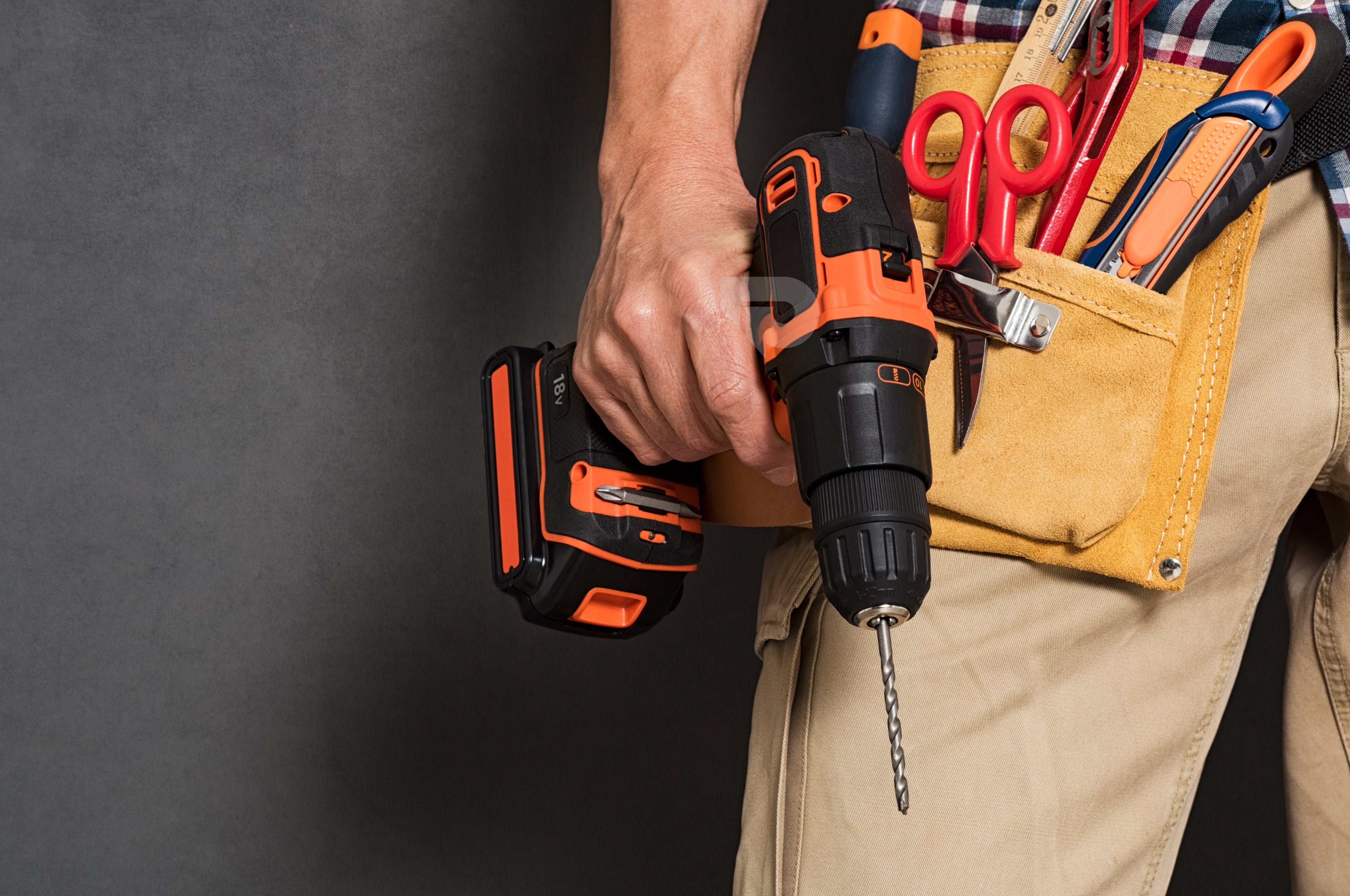 Close-up of a cordless power drill with a precision screwdriver bit, accompanied by an organized set of interchangeable bits in an orange holder on a black surface