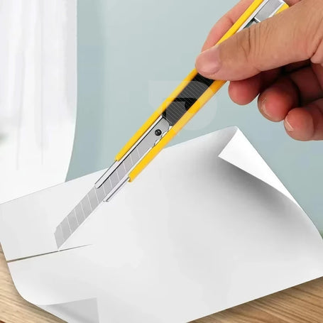 Person using a yellow utility knife to cut white paper on a light blue background.