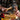 Close-up of a craftsman’s hands using a wooden-handled hammer to drive a nail into a wooden plank, surrounded by measuring tape, brush, and other woodworking tools.  